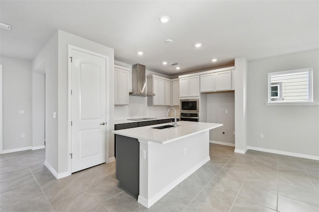 kitchen with built in microwave, sink, oven, a kitchen island with sink, and wall chimney exhaust hood