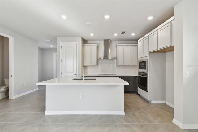 kitchen with gray cabinets, sink, a kitchen island with sink, black appliances, and wall chimney exhaust hood