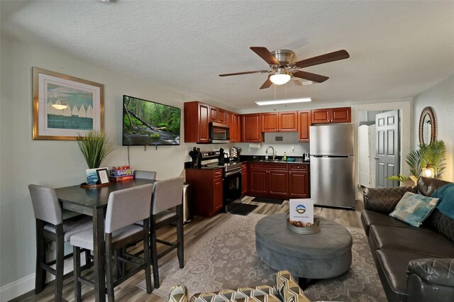 kitchen featuring ceiling fan, sink, stainless steel appliances, light hardwood / wood-style floors, and a textured ceiling