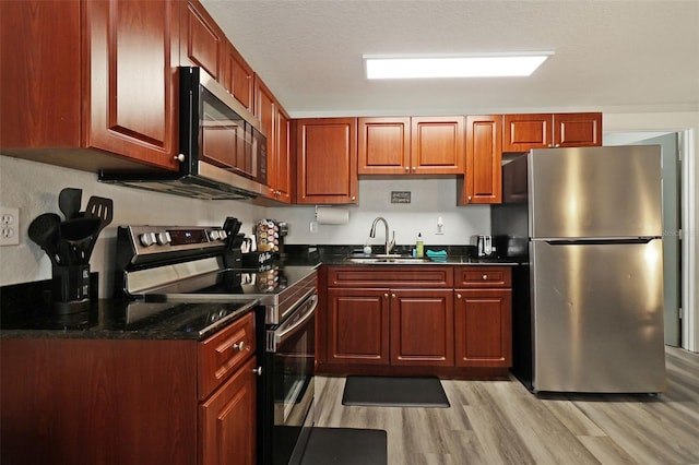 kitchen with dark stone counters, sink, light wood-type flooring, a textured ceiling, and stainless steel appliances