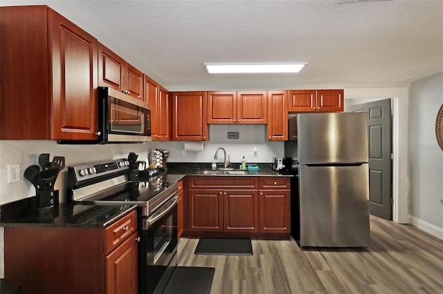 kitchen featuring sink, light hardwood / wood-style floors, a textured ceiling, and appliances with stainless steel finishes