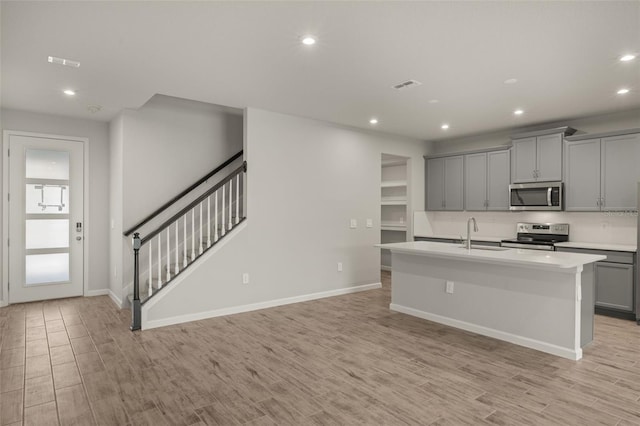 kitchen featuring sink, light hardwood / wood-style floors, gray cabinets, a center island with sink, and appliances with stainless steel finishes