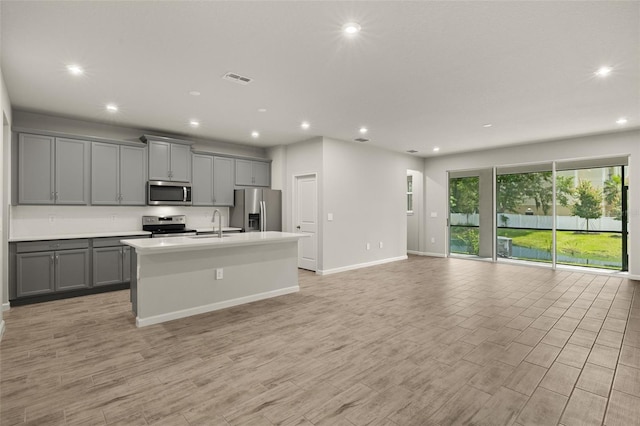 kitchen featuring light wood-type flooring, stainless steel appliances, gray cabinets, and a kitchen island with sink