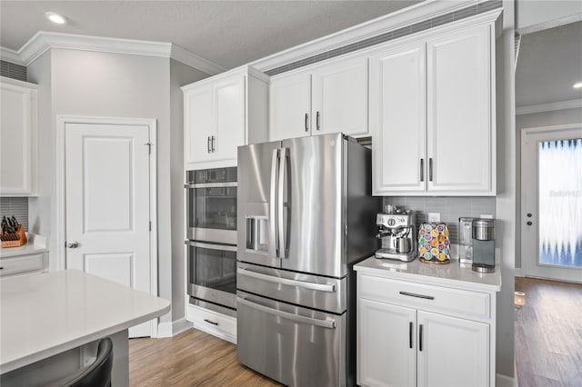 kitchen featuring decorative backsplash, white cabinets, stainless steel appliances, and wood-type flooring