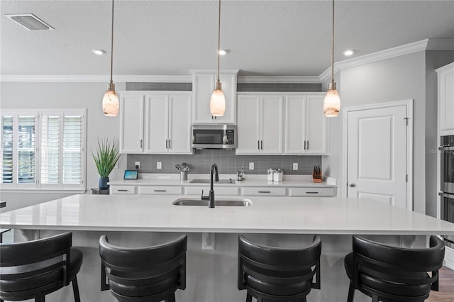 kitchen featuring a center island with sink, white cabinetry, hanging light fixtures, and sink