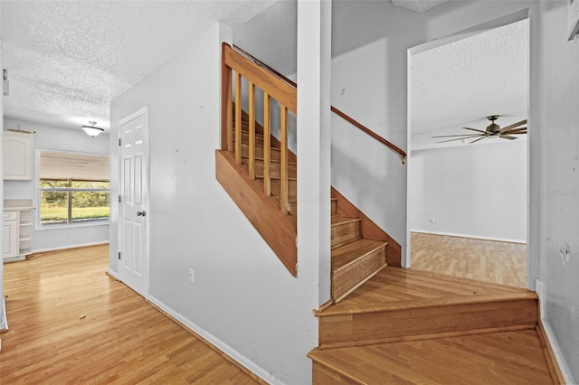 stairway with hardwood / wood-style flooring, ceiling fan, and a textured ceiling