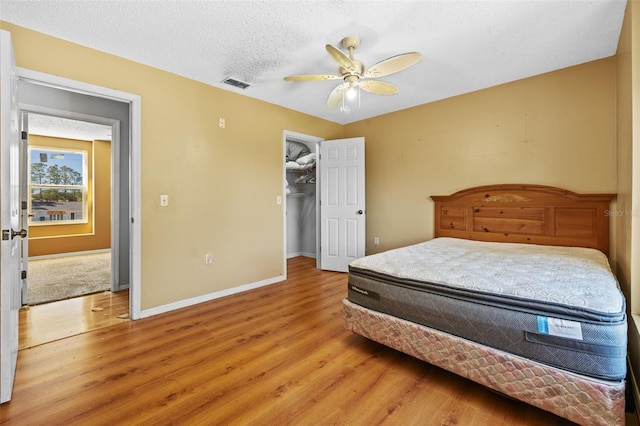 bedroom featuring ceiling fan, a spacious closet, a textured ceiling, and light wood-type flooring