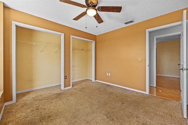 unfurnished bedroom with ceiling fan, carpet floors, a textured ceiling, and two closets