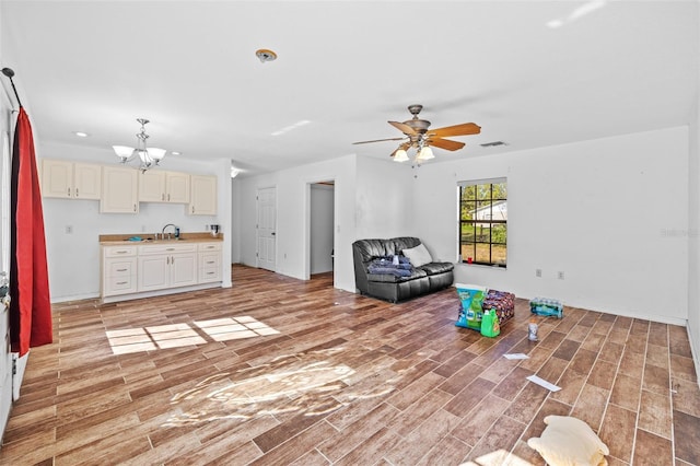 unfurnished living room featuring ceiling fan with notable chandelier and light hardwood / wood-style floors