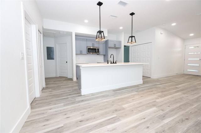 kitchen with hanging light fixtures, electric panel, an island with sink, and light wood-type flooring