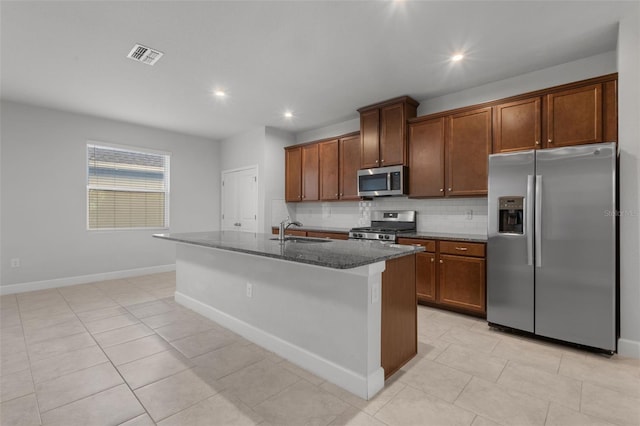 kitchen featuring sink, dark stone countertops, an island with sink, appliances with stainless steel finishes, and tasteful backsplash