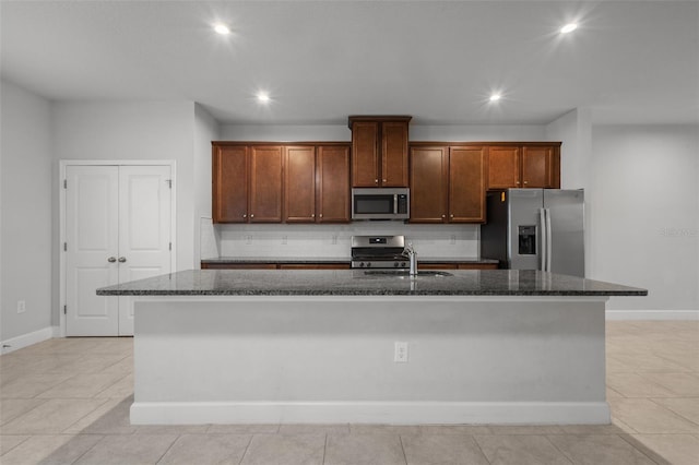 kitchen featuring appliances with stainless steel finishes, sink, dark stone counters, and an island with sink