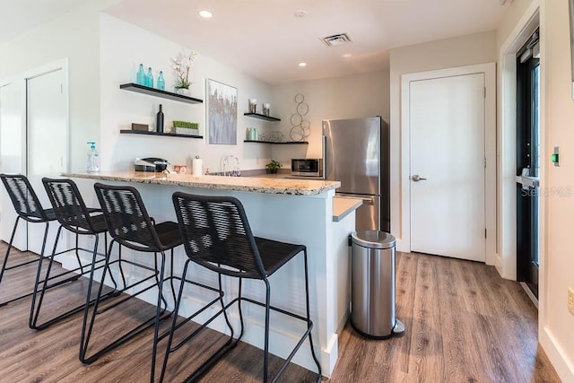 kitchen with a breakfast bar, wood-type flooring, kitchen peninsula, and appliances with stainless steel finishes