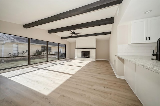 unfurnished living room featuring a fireplace, vaulted ceiling with beams, light hardwood / wood-style flooring, and ceiling fan