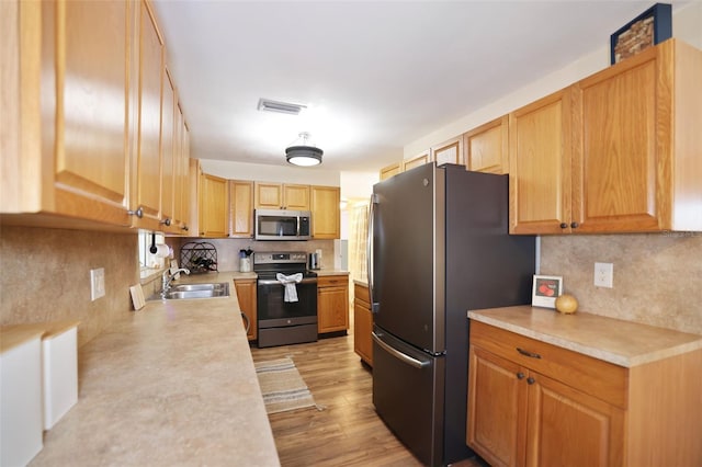 kitchen with appliances with stainless steel finishes, decorative backsplash, light hardwood / wood-style floors, and sink