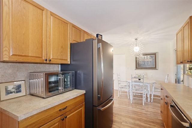 kitchen with light wood-type flooring, appliances with stainless steel finishes, pendant lighting, and a notable chandelier