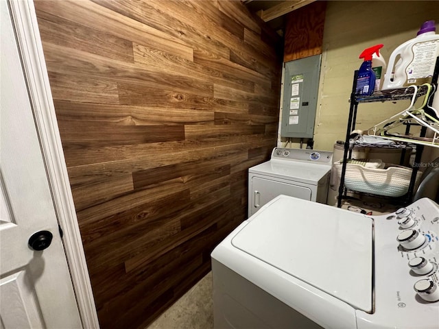 washroom with wooden walls, washing machine and clothes dryer, and electric panel