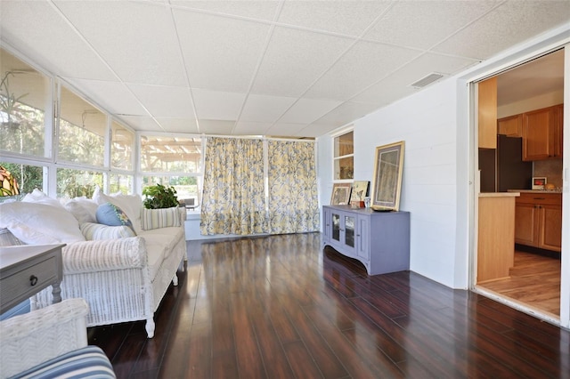 living room featuring dark wood-type flooring, plenty of natural light, a drop ceiling, and a wall of windows