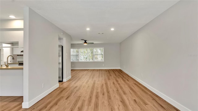 unfurnished living room with ceiling fan, light wood-type flooring, and sink