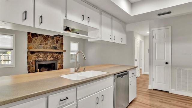 kitchen featuring sink, stainless steel dishwasher, light wood-type flooring, a fireplace, and white cabinetry