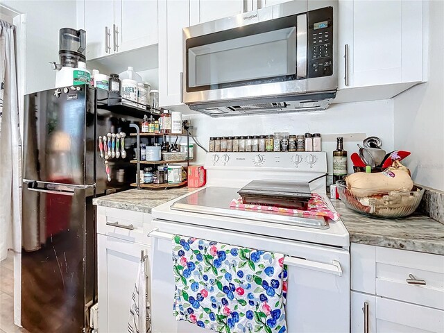 kitchen featuring white cabinets, white electric range, and black fridge