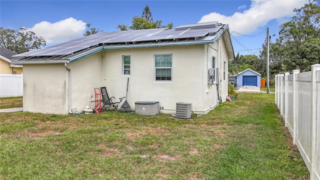 back of house with a yard, solar panels, central air condition unit, a garage, and an outbuilding