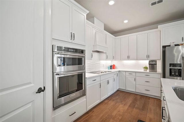 kitchen with white cabinetry, tasteful backsplash, hardwood / wood-style floors, appliances with stainless steel finishes, and custom exhaust hood