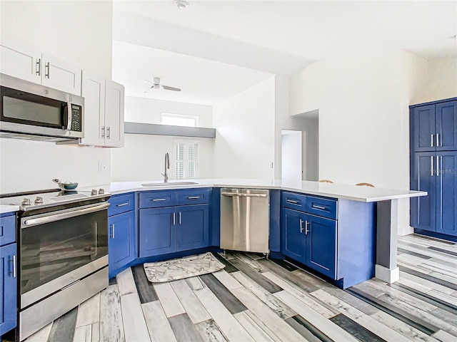 kitchen featuring blue cabinets, sink, kitchen peninsula, stainless steel appliances, and light hardwood / wood-style floors