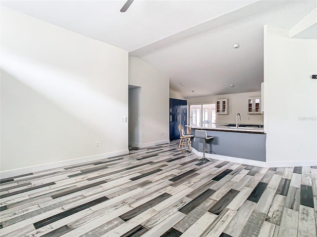 unfurnished living room with lofted ceiling, sink, ceiling fan, and light hardwood / wood-style flooring