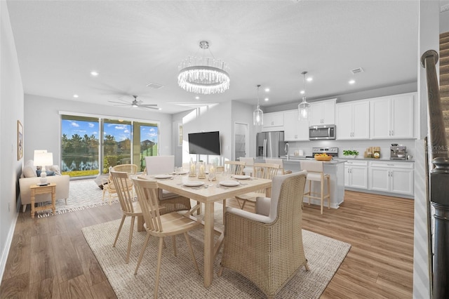 dining area featuring ceiling fan with notable chandelier, light hardwood / wood-style flooring, and sink