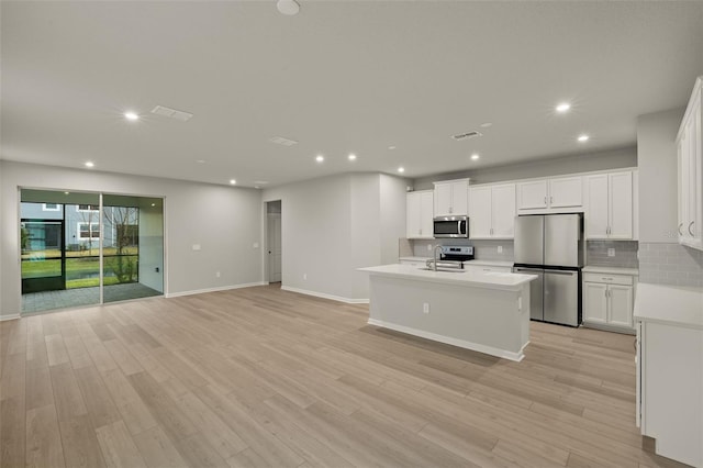 kitchen featuring stainless steel appliances, an island with sink, white cabinets, and light hardwood / wood-style floors