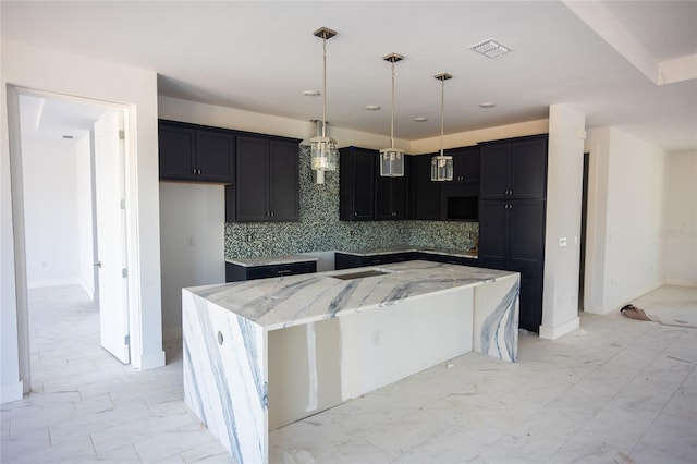 kitchen with tasteful backsplash, light stone countertops, a kitchen island, and decorative light fixtures