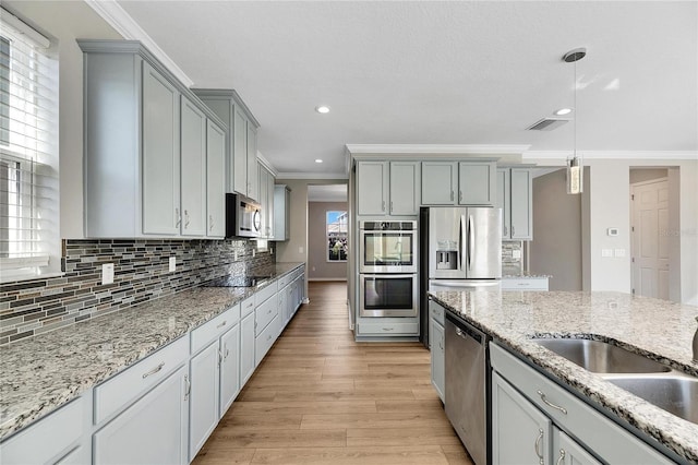 kitchen featuring appliances with stainless steel finishes, ornamental molding, gray cabinetry, light hardwood / wood-style flooring, and hanging light fixtures