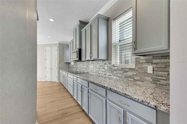 kitchen featuring light stone countertops, light wood-type flooring, backsplash, ornamental molding, and gray cabinetry