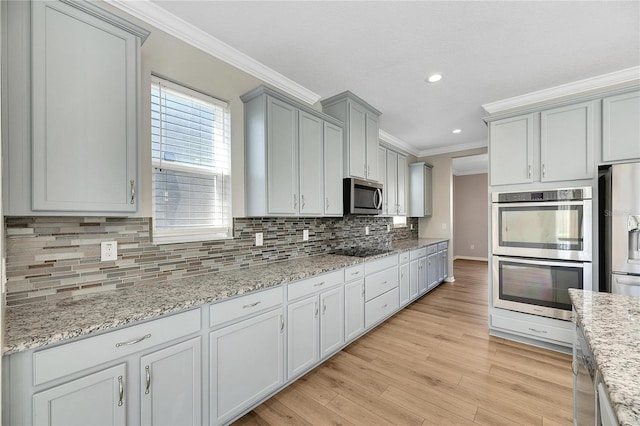 kitchen featuring light wood-type flooring, backsplash, light stone counters, stainless steel appliances, and crown molding