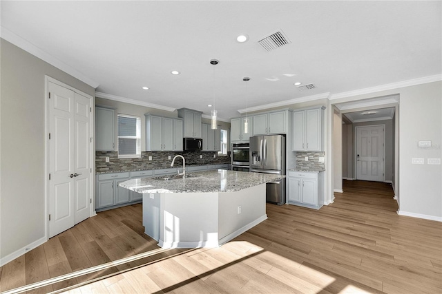 kitchen featuring light hardwood / wood-style floors, stainless steel appliances, hanging light fixtures, and an island with sink