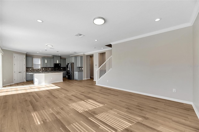 unfurnished living room featuring light hardwood / wood-style floors, crown molding, and sink