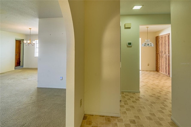 hallway featuring a notable chandelier and light carpet