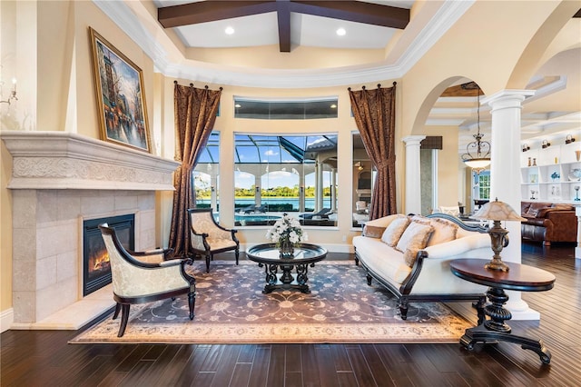 living area featuring hardwood / wood-style floors, a towering ceiling, ornate columns, beamed ceiling, and a tiled fireplace