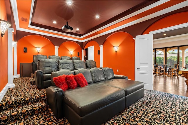 home theater room with decorative columns, a tray ceiling, crown molding, and carpet flooring