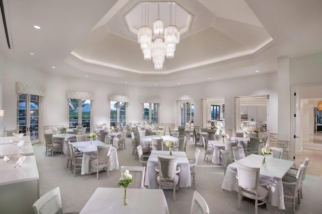 dining room featuring light carpet, a chandelier, a towering ceiling, and a raised ceiling