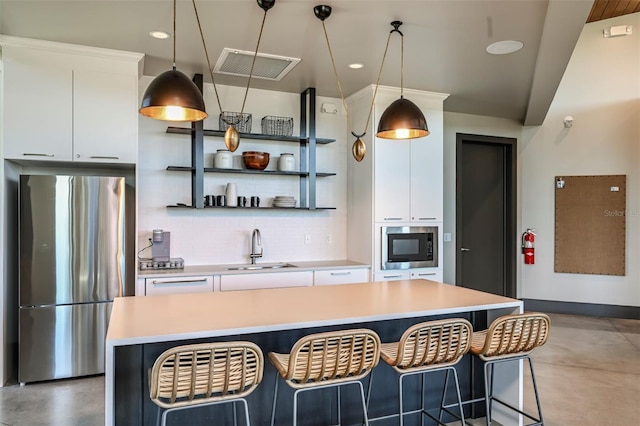 kitchen featuring stainless steel refrigerator, white cabinetry, sink, and hanging light fixtures