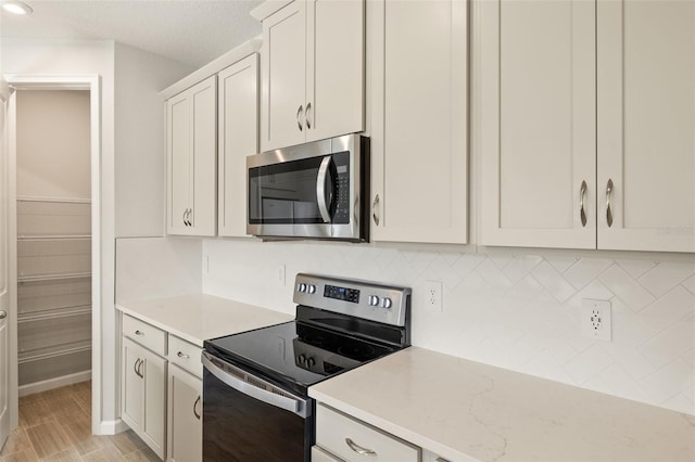 kitchen featuring white cabinetry, decorative backsplash, appliances with stainless steel finishes, and light stone counters