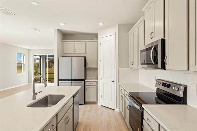 kitchen with tasteful backsplash, sink, light stone counters, and appliances with stainless steel finishes