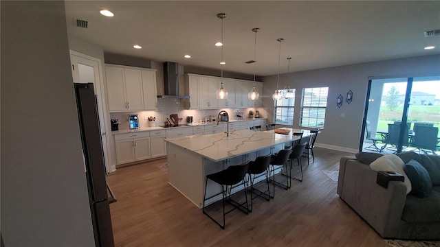 kitchen with white cabinetry, a large island, wall chimney exhaust hood, pendant lighting, and a breakfast bar area