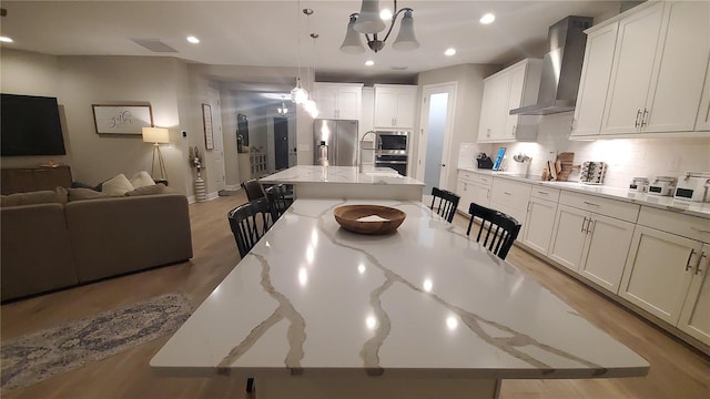 kitchen featuring wall chimney range hood, decorative light fixtures, light stone countertops, a large island, and stainless steel appliances