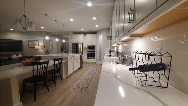 kitchen featuring white cabinets, light hardwood / wood-style floors, light stone counters, and hanging light fixtures