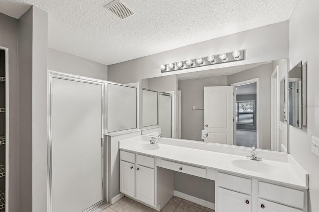 bathroom with tile patterned flooring, vanity, a shower with shower door, and a textured ceiling