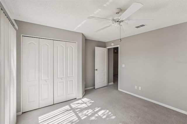 unfurnished bedroom with ceiling fan, a closet, light colored carpet, and a textured ceiling