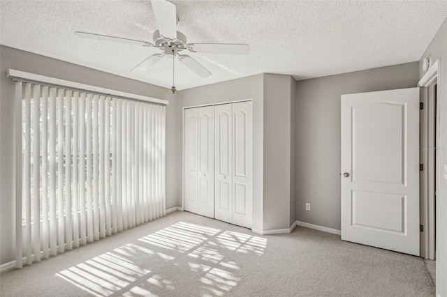 unfurnished bedroom with ceiling fan, a closet, light colored carpet, and a textured ceiling